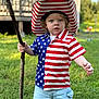 child, toddler, boy, grass, outdoor, stick, hat, american_flag, shirt, shorts, summer, portrait, curly_hair, blue_eyes, casual_clothing, nature, daylight, person, standing, expression