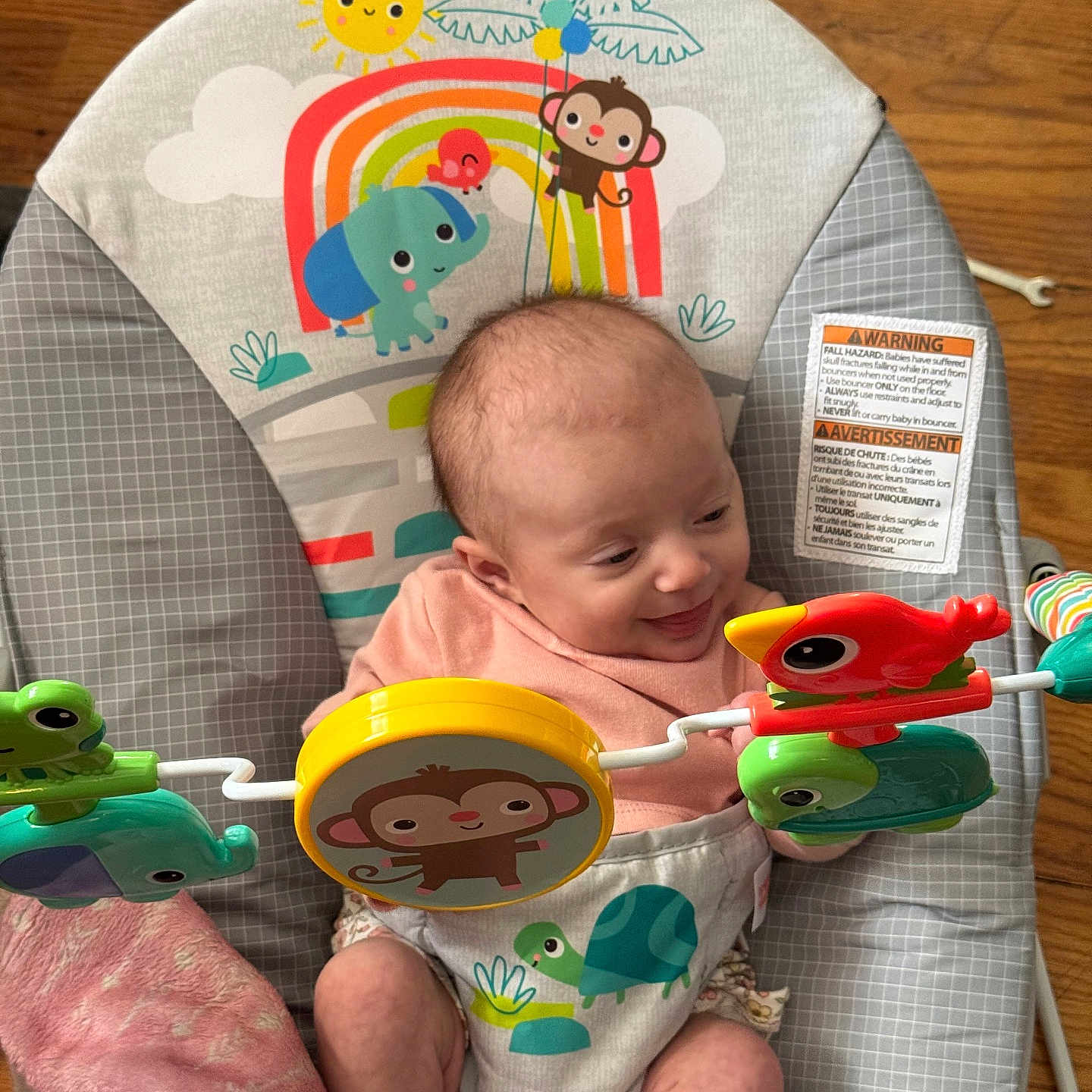 Emmerlyn is registered to the contest to win money with this photo: animal_illustration, baby, bouncer, child, clothing, colorful, comfort, cute, face, furniture, happy, indoor, infant, person, pink_blanket, playtime, smile, toddler, toy, wooden_floor