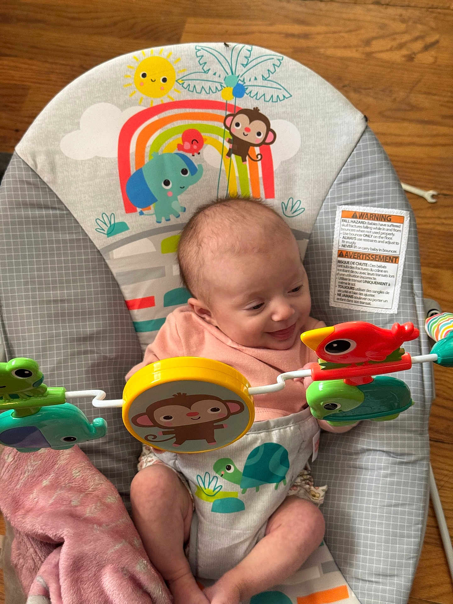 Emmerlyn is registered to the contest to win money with this photo: baby, infant, bouncer, toy, smile, happy, animal_illustration, colorful, wooden_floor, pink_blanket, clothing, face, child, cute, indoor, playtime, toddler, furniture, person, comfort