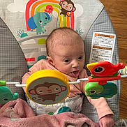 Emmerlyn is registered to the contest to win money with this photo: baby, infant, tongue_out, bouncer, toy, monkey, elephant, bird, turtle, blanket, wooden_floor, cute, child, playtime, colorful, soft, indoors, smiling, happy, person