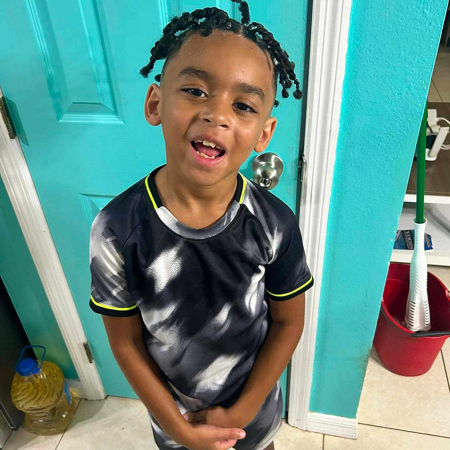 Nicholas is registered to the contest to win money with this photo: boy, braided_hair, bucket, casual, child, cleaning_supplies, door, happy, home, indoors, mop, playful, portrait, shorts, smiling, sneakers, standing, tile_floor, tshirt, young