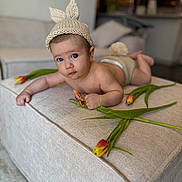 Arthur joined the competition — help win amazing prizes! baby, infant, knitted_hat, bunny_ears, tulips, flower, ottoman, beige, indoor, living_room, cute, child, portrait, soft_lighting, couch, home_decor, laying_down, curious, expression, hand