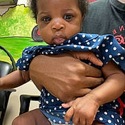 Sariyah is registered to the contest to win money with this photo: baby, child, infant, polka_dot, blue_clothing, hand, adult, holding, indoor, mural, colorful, curly_hair, diaper, seated, person, face, cute, expression, portrait, skin