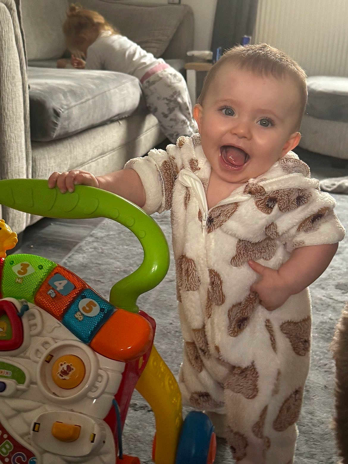 Toni-Louise joined the competition — help win amazing prizes! baby, child, toy, walker, onesie, animal_print, smiling, indoor, carpet, sofa, furniture, happy, person, play, toddler, couch, floor, hand, face, background