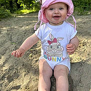Margot a rejoint le concours — aidez-le/la à gagner de superbes lots ! baby, child, pink_hat, onesie, bunny_print, smiling, sand, outdoor, nature, greenery, sunlight, happy, cute, sitting, young_child, summer, playful, portrait, headwear, barefoot