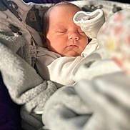 Amira joined the competition — help win amazing prizes! baby, infant, newborn, sleeping, blanket, bedding, swaddle, sock, face, closed_eyes, peaceful, cozy, portrait, closeup, soft_light, nursery, blanket_pattern, nap, cute, bokeh