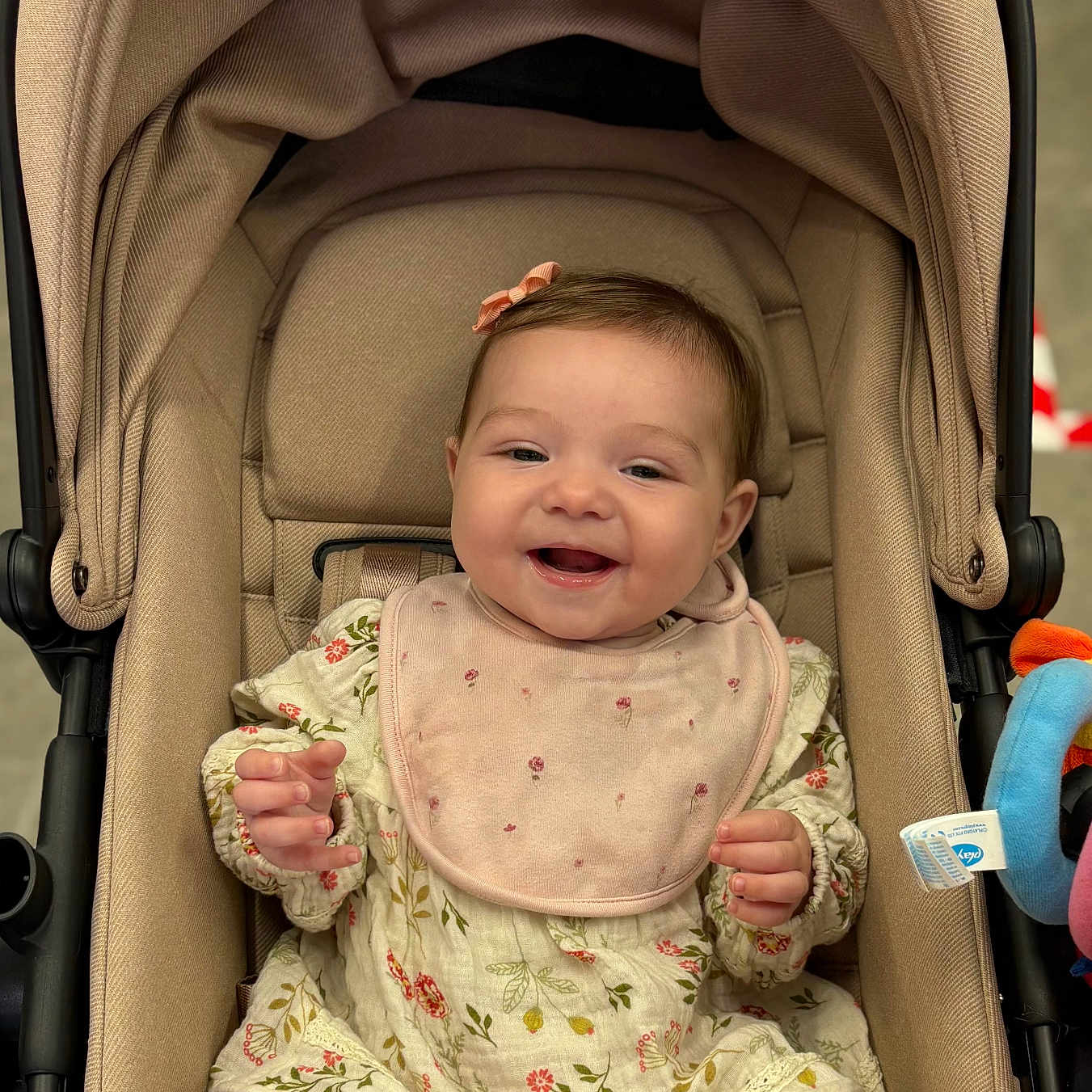Emila joined the competition — help win amazing prizes! baby, child, clothing, comfort, cute, fabric, floral_dress, happy, headwear, indoors, infant, legs, person, pink_bib, plaything, portrait, seat, smiling, stroller, toy