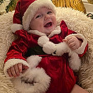 Honey is registered to the contest to win money with this photo: baby, child, christmas, santa_claus, holiday, festive, smiling, happy, cute, red_clothing, hat, fur_trim, decorations, tree, lights, indoor, cushion, cozy, seasonal, portrait