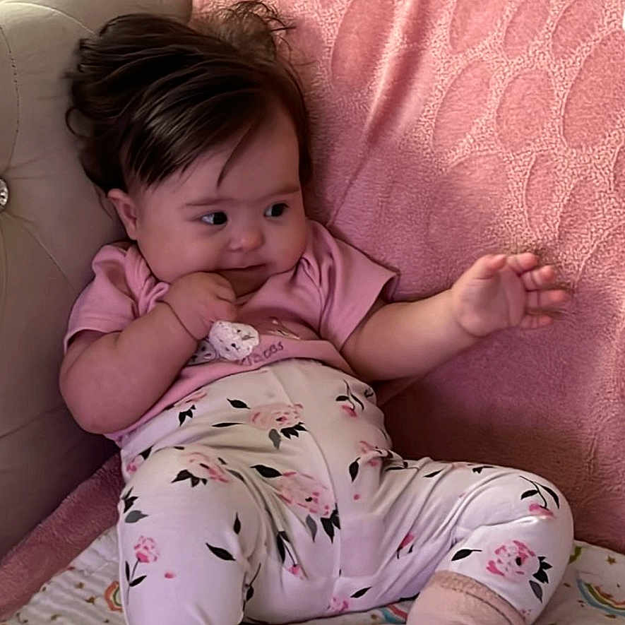 Yaren is registered to the contest to win money with this photo: baby, infant, pink_clothing, floral_pants, socks, blanket, rainbow_pattern, cushion, pillow, soft_furnishing, indoors, child, cute, sitting, portrait, person, young_child, home, relaxed, cozy