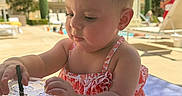 Michelle is registered to the contest to win money with this photo: baby, child, swimsuit, poolside, towel, plastic_cup, straw, summer, outdoor, sunny, curious, sitting, water, relaxation, vacation, person, infant, daylight, background, leisure