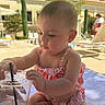 baby, child, swimsuit, poolside, towel, plastic_cup, straw, summer, outdoor, sunny, curious, sitting, water, relaxation, vacation, person, infant, daylight, background, leisure
