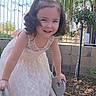 Hana is registered to the contest to win money with this photo: child, girl, toddler, smiling, portrait, outdoor, garden, backyard, dress, white_dress, bow, curly_hair, shoes, sparkly_shoes, slide, playground, fence, tree, flowers, daylight