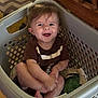 baby, child, laundry_basket, smiling, drool, brown_shirt, indoor, wooden_furniture, carpet, clothing, cute, happy, person, sitting, household, playful, infant, face, tongue_out, casual