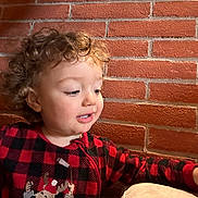 Samuel a rejoint le concours — aidez-le/la à gagner de superbes lots ! child, toddler, curly_hair, red_onesie, checkered_pattern, reindeer_design, brick_wall, indoor, hand, cute, portrait, smiling, baby, face, person, young_child, warm_lighting, cozy, clothing, curious