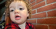 Samuel a rejoint le concours — aidez-le/la à gagner de superbes lots ! child, toddler, curly_hair, red_clothing, checkered_pattern, face, expression, indoor, brick_wall, background, clothing, person, portrait, close_up, young_child, casual, curious, head_and_shoulders, indoor_lighting