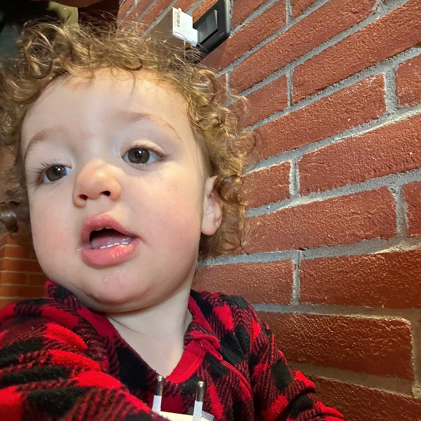 Samuel a rejoint le concours — aidez-le/la à gagner de superbes lots ! child, toddler, curly_hair, red_clothing, checkered_pattern, face, expression, indoor, brick_wall, background, clothing, person, portrait, close_up, young_child, casual, curious, head_and_shoulders, indoor_lighting