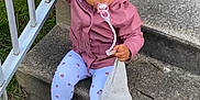 Lilena participe au concours pour gagner de l'argent avec cette photo : toddler, child, pacifier, stairs, concrete, railing, curly_hair, pink_jacket, leggings, white_shoes, outdoor, grass, toy, holding, sitting, curious, person, footwear, clothing, daylight