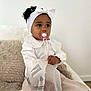 Lilena a rejoint le concours — aidez-le/la à gagner de superbes lots ! toddler, child, pacifier, headband, white_clothing, beige_pants, plastic_bag, blanket, curly_hair, sitting, indoors, soft_lighting, young_child, cute, portrait, clothing, hand, face, expression, cozy