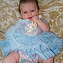 baby, infant, blue_tutu, floral_outfit, blanket, patterned_background, chubby_cheeks, hand, face, cute, sitting, soft_cloth, indoors, skin, head, legs, footwear, person, young_child, resting