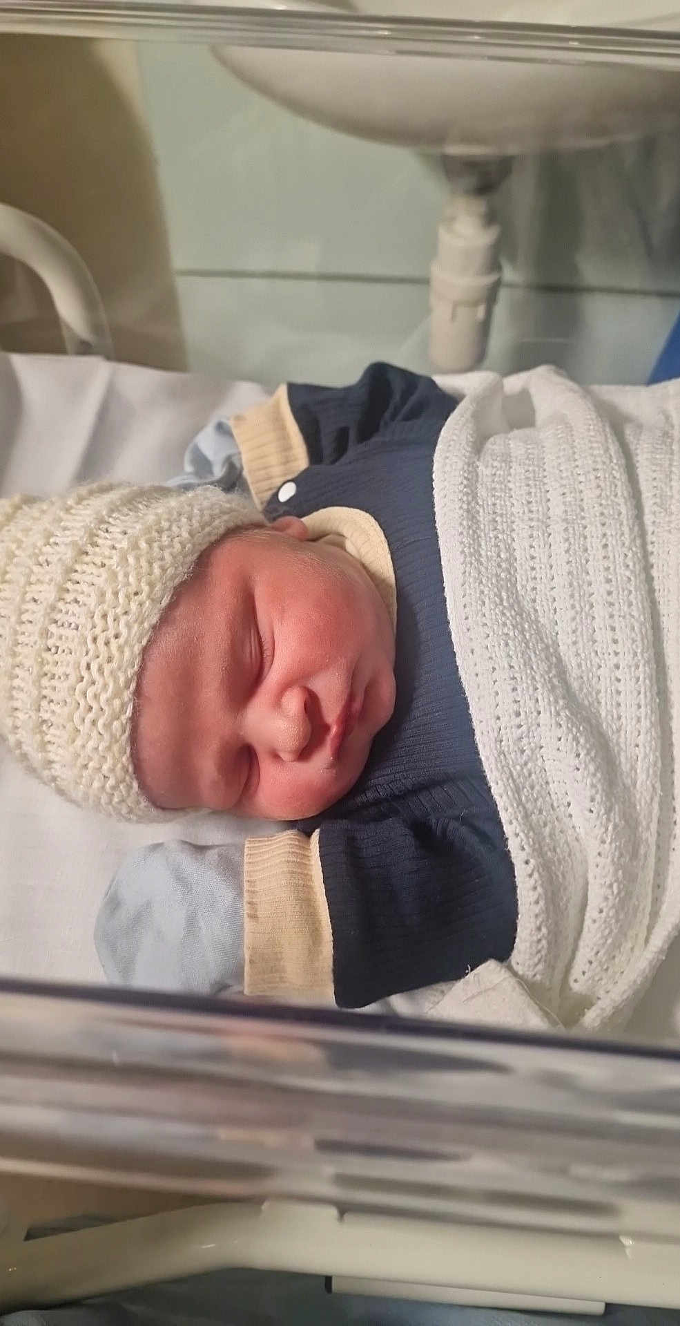 Arley is registered to the contest to win money with this photo: newborn, baby, sleeping, blanket, knit_hat, hospital, bassinet, infant, cozy, cute, soft_lighting, wrapped, clothing, person, portrait, peaceful, toddler, child, indoor, resting