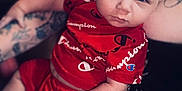 Victor is registered to the contest to win money with this photo: baby, infant, child, portrait, close_up, red_clothing, brand_champion, tattooed_arm, holding, cuddling, blue_eyes, chubby_cheeks, onesie, sitting, person, indoor, soft_lighting, serious_expression, cute, parent_arm