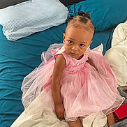 Kailani joined the competition — help win amazing prizes! toddler, child, pink_dress, bed, pillow, blanket, blue_sheets, person, indoors, hair_buns, young_child, looking_up, serious_expression, fabric, soft_toys, home, cute, sitting, portrait, casual