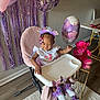toddler, birthday_girl, high_chair, balloon, purple_decorations, pink_teddy_bear, party, streamers, headband, smiling, indoor, table, floor_rug, white_shoes, butterfly_decor, clothing, celebration, child, person, happy