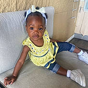 Raeyah joined the competition — help win amazing prizes! toddler, child, girl, yellow_dress, denim_shorts, white_sneakers, hair_bows, couch, indoor, portrait, curly_hair, casual_clothing, relaxed_pose, brown_skin, earrings, textured_wall, flooring, home_interior, cute, young_child