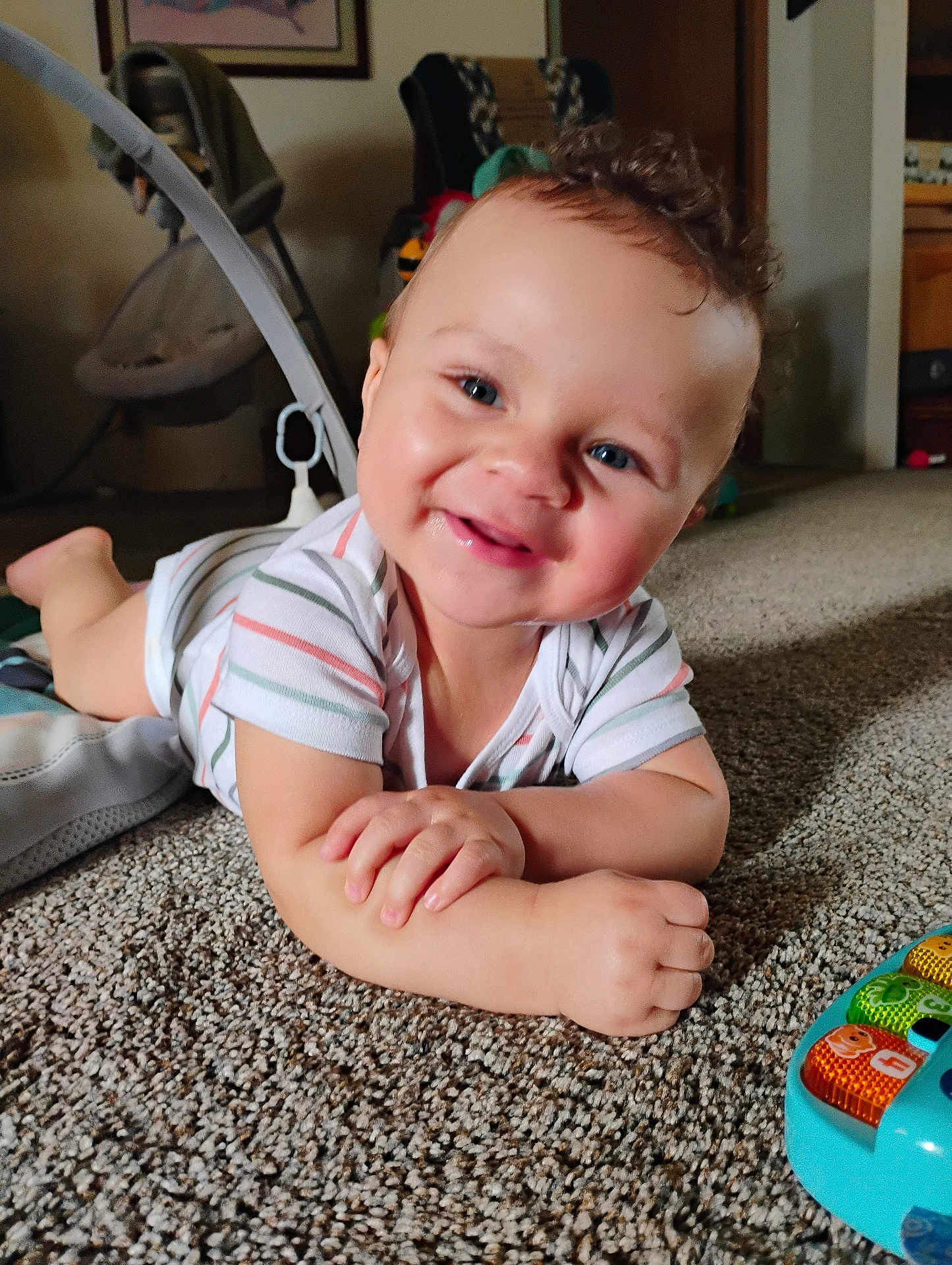 Jameson is registered to the contest to win money with this photo: baby, infant, smiling, curly_hair, carpet, toy, home_interior, child, face, happy, cute, toddler, clothing, floor, hands, blue_eyes, relaxed, indoor, portrait, playful
