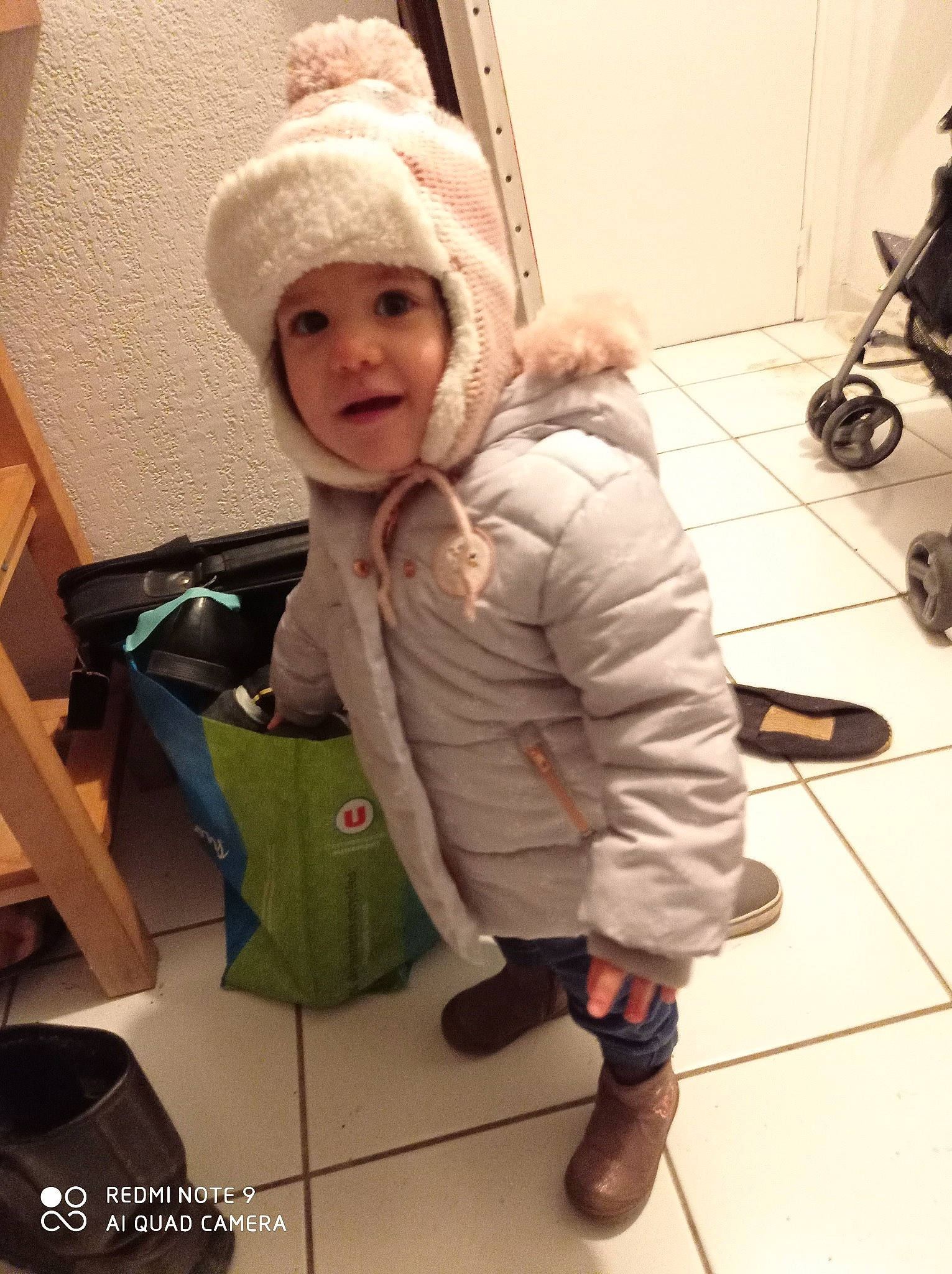 Jade a rejoint le concours — aidez-le/la à gagner de superbes lots ! baby, baby_toddler_clothing, bag, boot, cap, cheek, clothing, comfort, floor, flooring, fun, headwear, jacket, joint, luggage_and_bags, person, shoe, sitting, smile, toddler