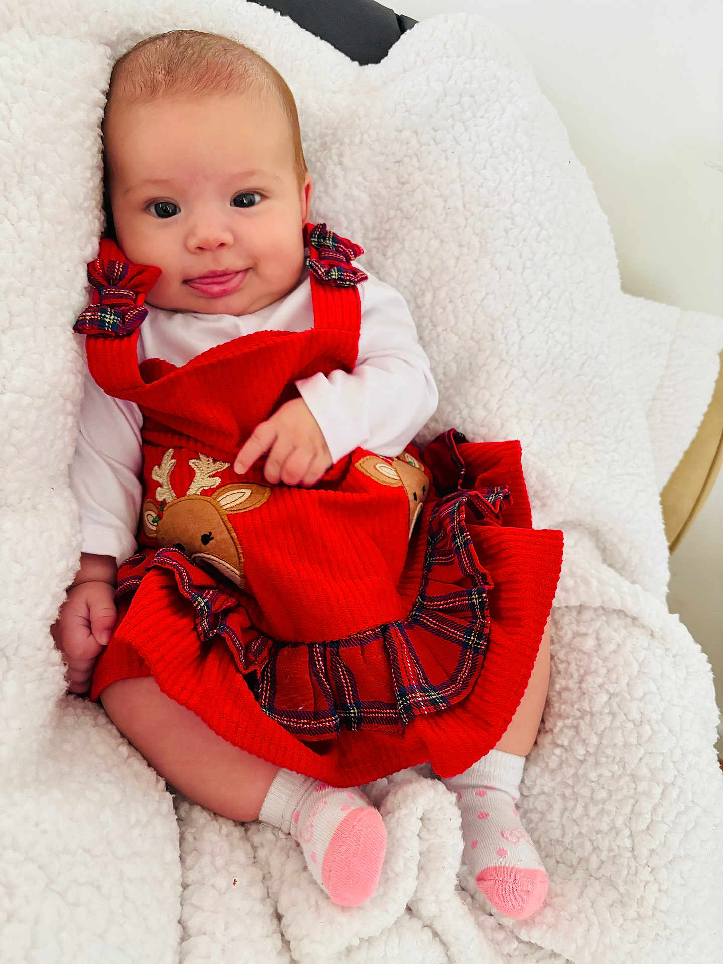 Génesis is registered to the contest to win money with this photo: baby, infant, red_dress, reindeer, plaid, white_blanket, cozy, cute, smiling, tongue_out, child, socks, soft_texture, indoor, portrait, happy, holiday, festive, person, seated