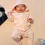 Génesis is registered to the contest to win money with this photo: baby, infant, child, pink_clothing, hooded_jacket, patterned_outfit, strawberry_print, lying_down, tongue_out, blanket, water_bottle, soft_surface, cute, smiling, indoors, cozy, socks, face, person, portrait