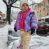 toddler, child, winter, snow, snowy_street, colorful_jacket, white_hat, mittens, snow_covered_car, residential_area, tree, sidewalk, curious_expression, outdoor, cold_weather, pants, sneakers, urban, daytime, person