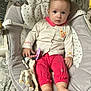 baby, baby_rocker, blue_eyes, child, clothing, comfort, cream_shirt, cute, face, feet, giraffe_toy, hands, indoor, infant, pacifier, patterned_bedspread, pink_pants, seat, short_hair, toy