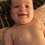 baby, bare_chest, bed, blanket, cheeks, child, closeup, cute, face, happy, indoors, infant, lying_down, person, pillow, portrait, relaxing, skin, smiling, young_child