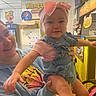 Jade is registered to the contest to win money with this photo: baby, child, woman, smile, bow, denim_overalls, indoor, restaurant, wall_art, yellow_tiles, person, holding, happy, cute, headband, clothing, hand, face, cheerful, casual