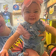 Jade joined the competition — help win amazing prizes! baby, child, person, denim_overalls, pink_bow, headband, hoodie, indoor, restaurant, hand, smile, face, tile_wall, yellow, cartoon, clock, menu, stroller, casual, holding