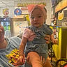 Jade joined the competition — help win amazing prizes! baby, child, person, headband, pink, denim, overalls, hand, smile, indoor, restaurant, yellow_tiles, signage, menu, counter, adult, holding, floor, stroller, pepsi
