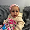 baby, child, pink_beanie, hoodie, blanket, toy, couch, indoor, cozy, curious, portrait, cute, infant, soft, comfortable, clothing, person, smiling, young, home