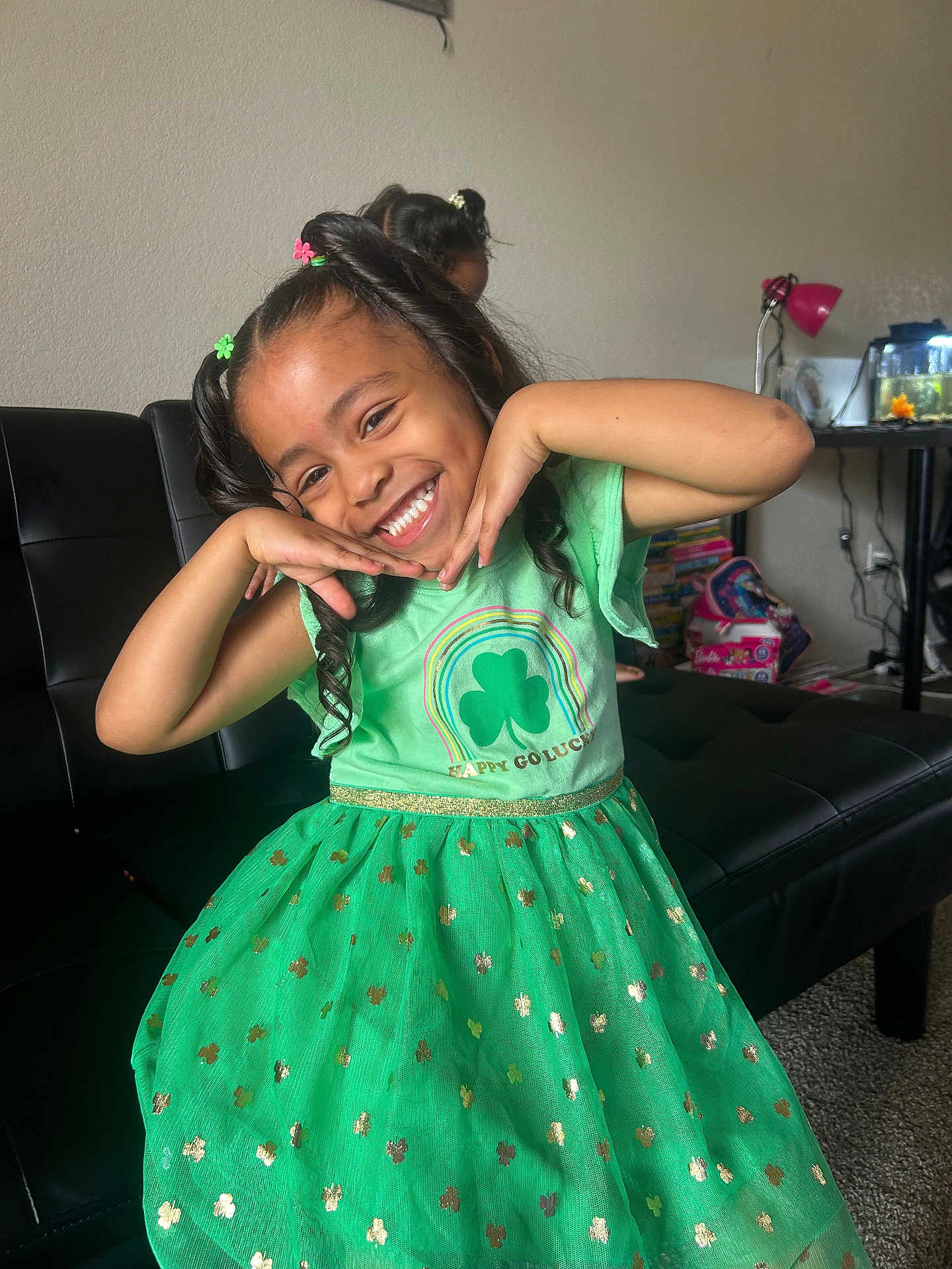Malieah is registered to the contest to win money with this photo: child, girl, smiling, green_dress, happy, indoor, posing, living_room, furniture, toys, books, curly_hair, playful, black_sofa, carpet, lamp, fish_tank, decor, cute, portrait
