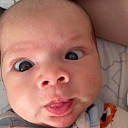 Branson is registered to the contest to win money with this photo: baby, face, close_up, expression, onesie, patterned_pillow, infant, tongue_out, wide_eyes, cute, child, sleepwear, head, skin, mouth, human, indoors, portrait, newborn, baby_clothing