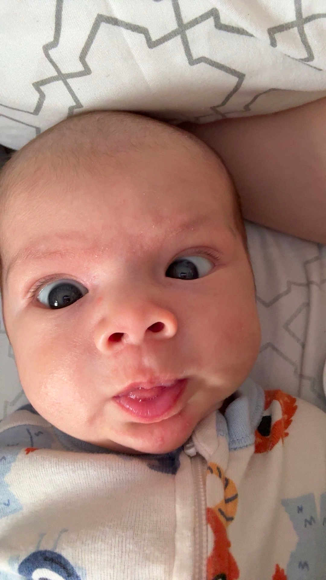 Branson is registered to the contest to win money with this photo: baby, face, close_up, expression, onesie, patterned_pillow, infant, tongue_out, wide_eyes, cute, child, sleepwear, head, skin, mouth, human, indoors, portrait, newborn, baby_clothing