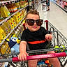 adult, aisle, child, clothing, floor, footwear, grocery, hat, person, plastic_bottle, product, retail, shelf, shopping, shopping_cart, store, sunglasses, supermarket, toddler, toy