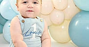 Louis is registered to the contest to win money with this photo: baby, balloons, birthday, blue_clothing, celebration, child, cute, decorations, event, happy, indoor, infant, one_year_old, pastel_colors, person, portrait, sitting, smiling, studio, young_child