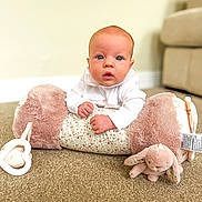 Larna joined the competition — help win amazing prizes! baby, infant, child, carpet, plush_pillow, soft_toy, floor, indoor, blue_eyes, white_clothing, curious_expression, hands, couch, blurred_background, home, cozy, face, portrait, cute, toddler
