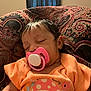 baby, sleeping, pacifier, orange_shirt, mushroom_design, patterned_cushion, indoor, child, infant, peaceful, cute, face, person, clothing, resting, head, portrait, young, cozy, comfort