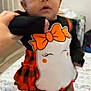 baby, child, costume, ghost, orange_bow, headband, plaid, bed, blanket, hand, indoor, person, face, video_call, smile, holding, foot, curly_hair, clothing, toddler
