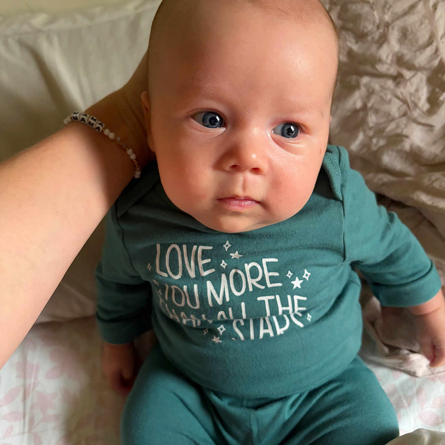 Caissian is registered to the contest to win money with this photo: baby, infant, child, portrait, sitting, bed, bedding, pillow, blanket, teal_clothing, onesie, wide_eyes, blue_eyes, serious_expression, indoor, bedroom, adult_arm, close_up, photograph, safe