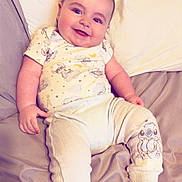 Jaxson is registered to the contest to win money with this photo: baby, smiling, pajamas, bed, pillow, infant, child, cute, happy, lying_down, indoors, person, sleepwear, plush, soft, comfort, relaxed, cartoon, foot, face