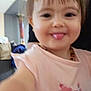 toddler, child, face, smiling, tongue_out, pink_shirt, floral_design, indoor, person, happy, closeup, blurry, hair, head, playful, young_child, casual_clothing, portrait, cute, baby
